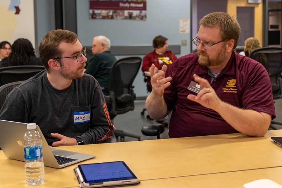 A faculty member sitting with a student at a table.