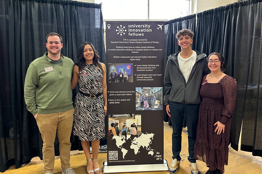 A group of four students standing in front of a banner for the University Innovation Fellows program.