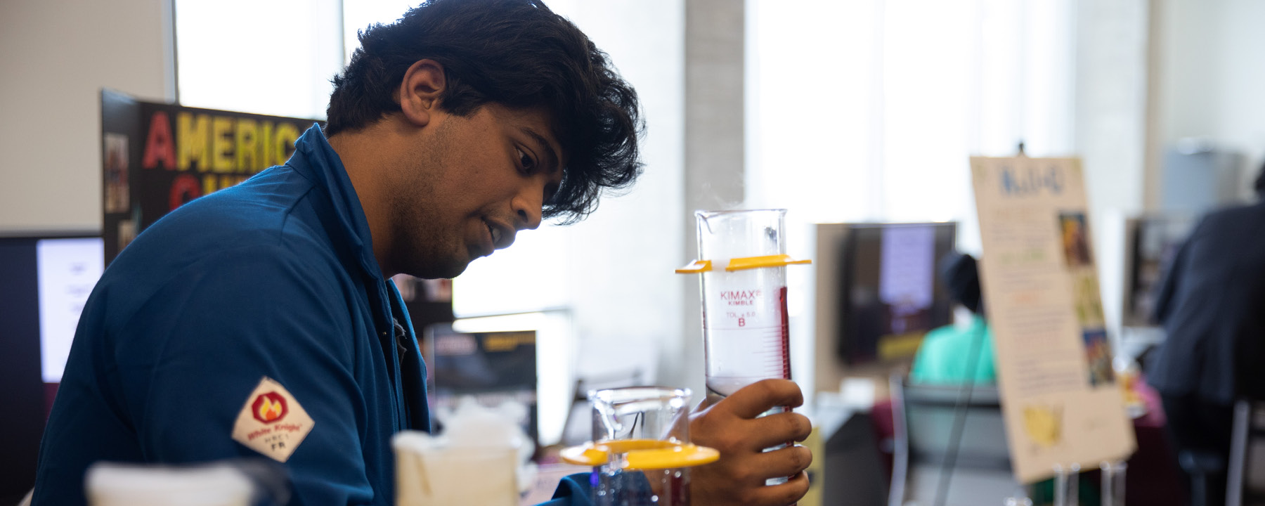 A student in a blue lab coat holding a beaker.