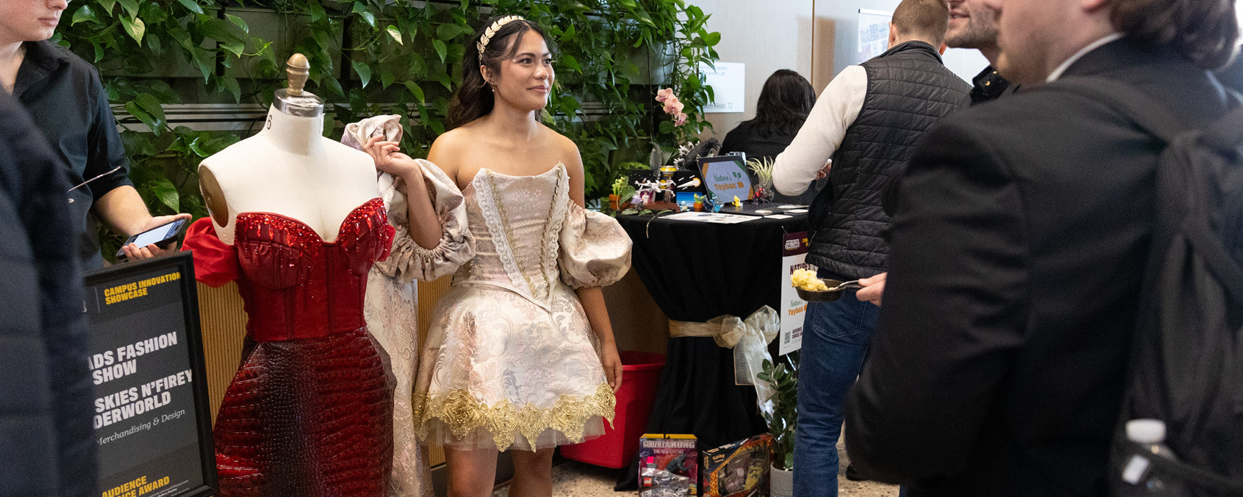 A student standing next to a mannequin showcasing her fashion designs at the New Venture Challenge Innovation Showcase.