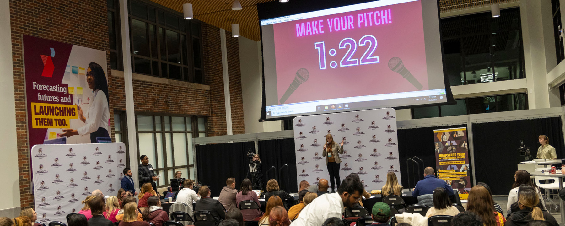 A student pitching on stage in front of a crowd with a timer behind her counting down.