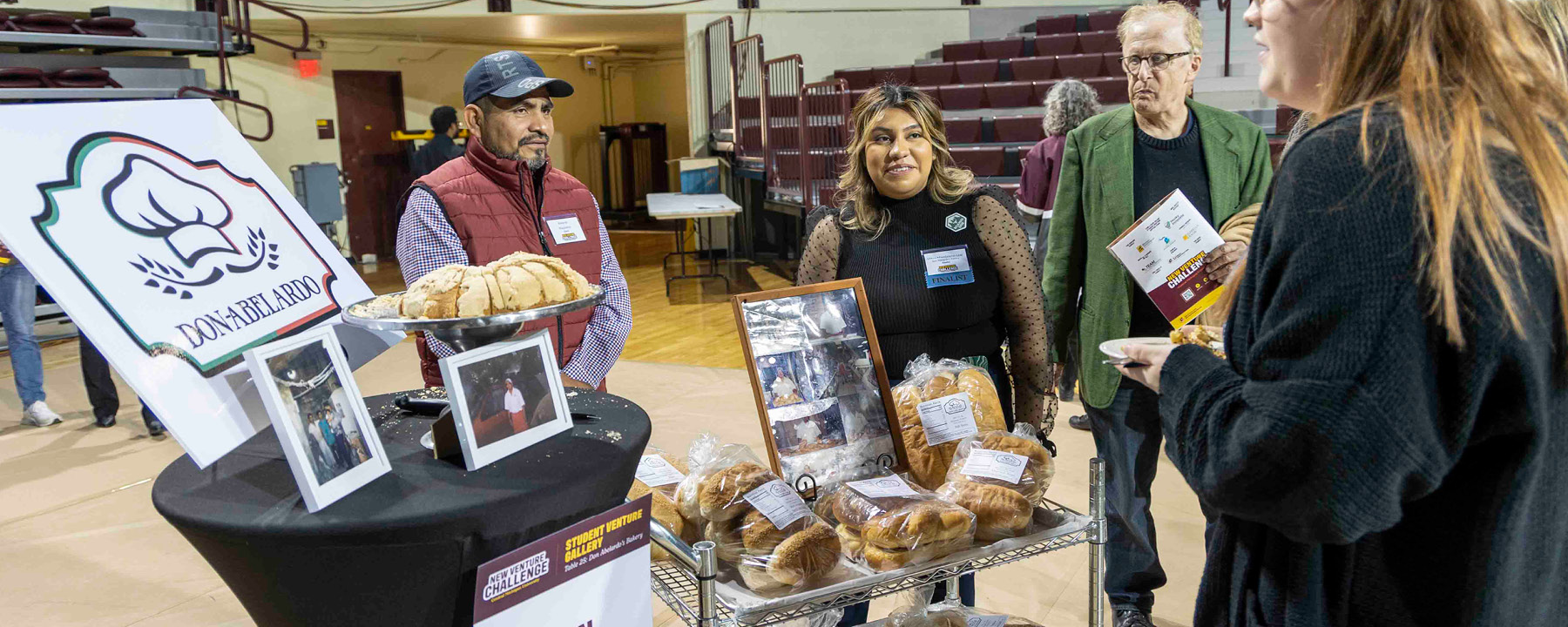 Four adults standing next to a table display of a bakery at the 2023 New Venture Challenge.