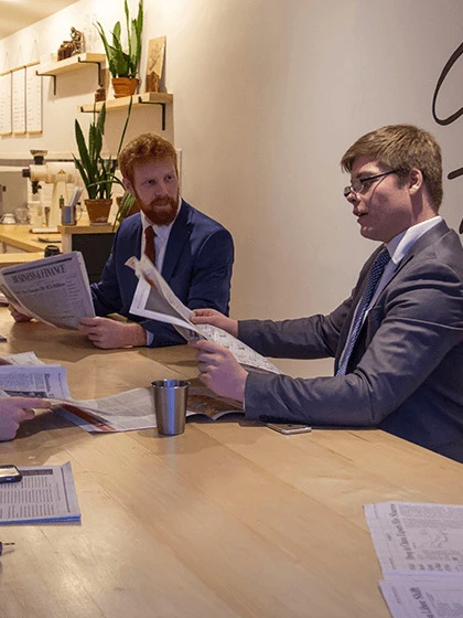 a group of men sitting at a table reading newspaper