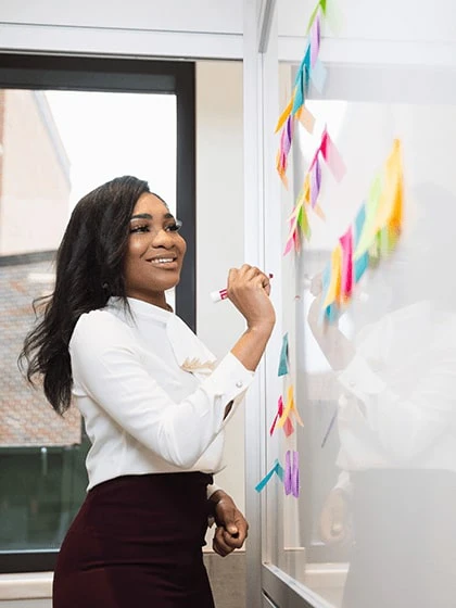 A woman in business attire writing on a whiteboard and smiling.