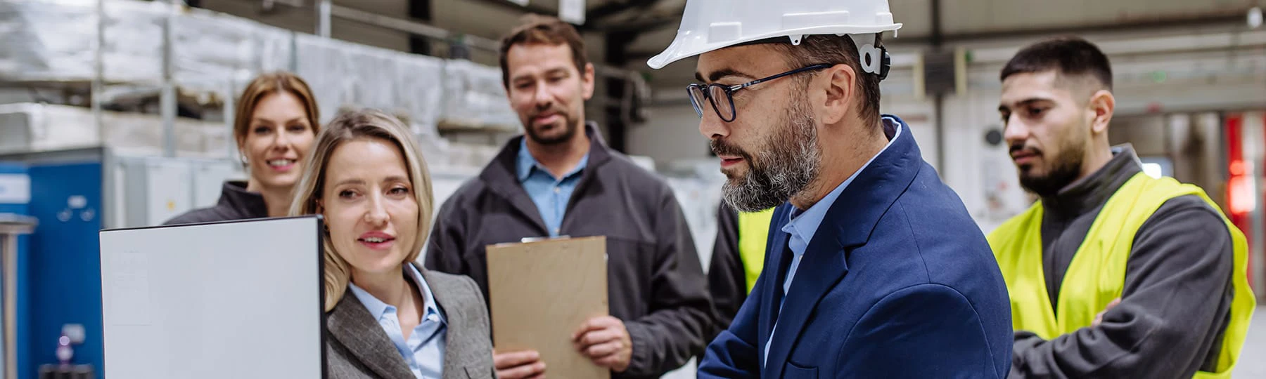 A group of female and male logisticians look at a computer screen while standing in a warehouse.