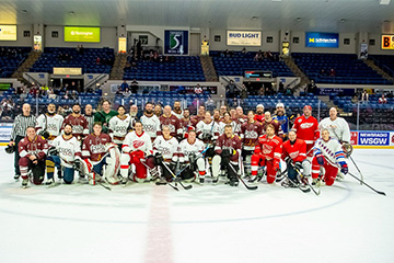 Large group of men and women in hockey gear pose for the camera at center ice.