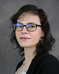 A woman wearing glasses and a black shirt smiles for a professional headshot.