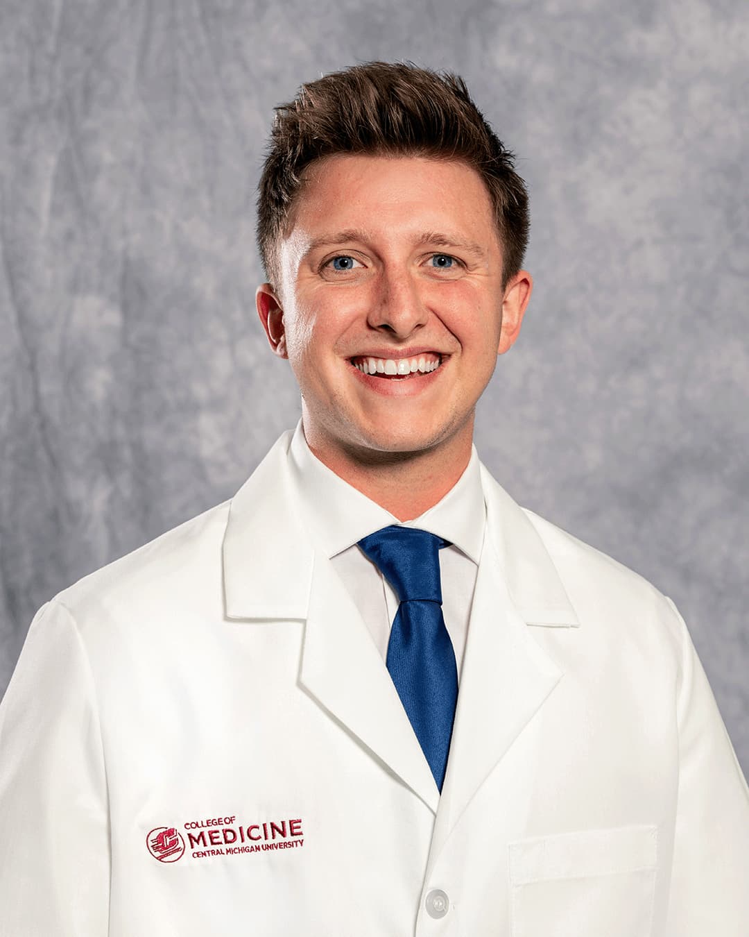 Book, Ethan 200 x 250 web A male CMU College of Medicine medical student wearing his white coat as he smiles for the camera.