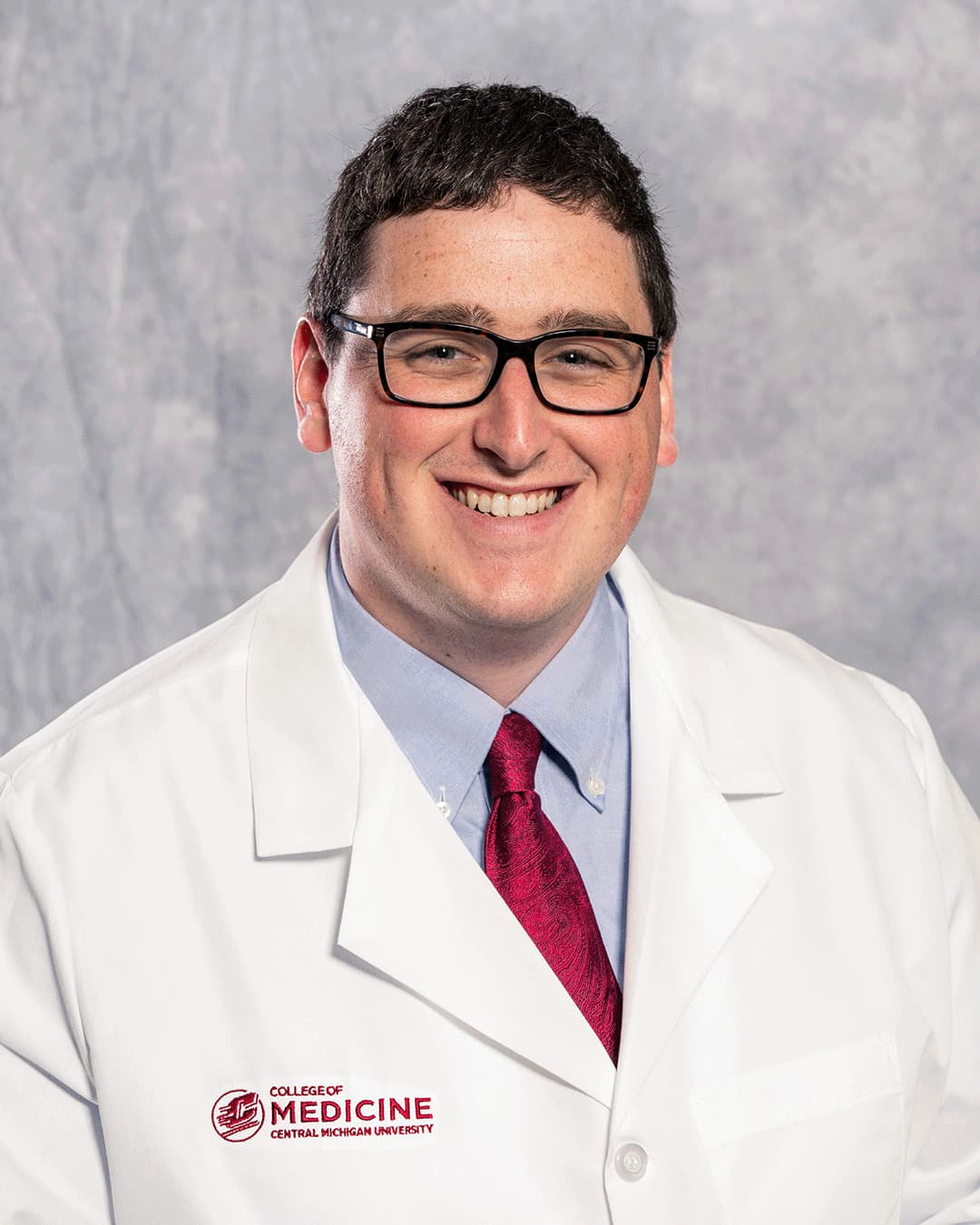 Byrne, John 200 x 250 web A male CMU College of Medicine medical student with rectangular black glasses is wearing his white coat as he smiles for the camera.