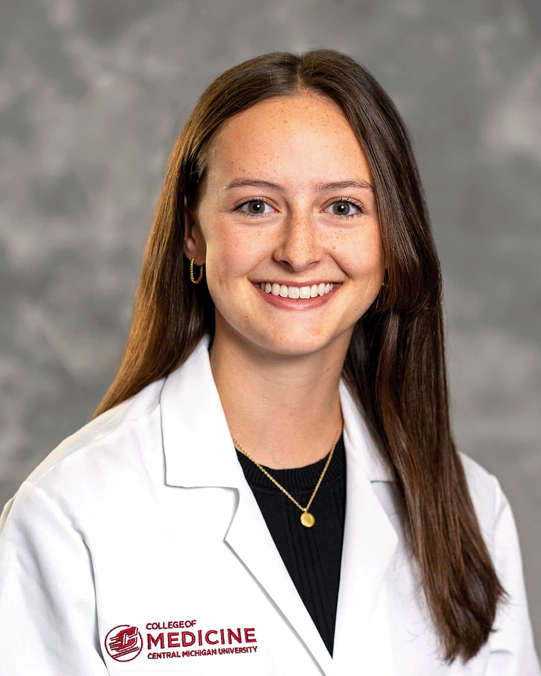 Harber, Isabelle 200 x 250 web A female CMU College of Medicine medical student with long brown hair wearing her white coat over a black blouse as she smiles for the camera.