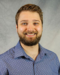 Headshot of Michael Bernard wearing a blue and white patterned dress shirt.