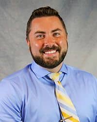 Headshot of Daniel Dunaske wearing a blue dress shirt and a blue, yellow and white striped necktie.