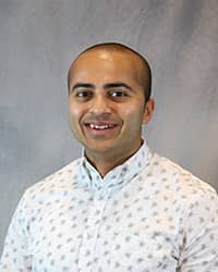 Headshot of Rabshen Rahman wearing a white button up top with green shapes.