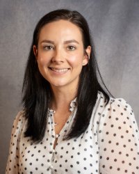 A women with long dark hair smiling while wearing a white polka dot blouse.