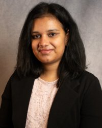 A women with long dark hair wearing a dark suit with a pink blouse.