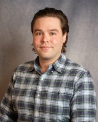 A man with short brown hair wearing a plaid collared shirt.