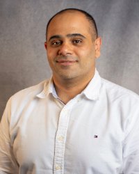 A man in a white shirt smiles for a professional headshot in front of a grey background.