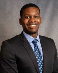 A man in a black suit, blue patterned shirt, and blue and black striped tie.