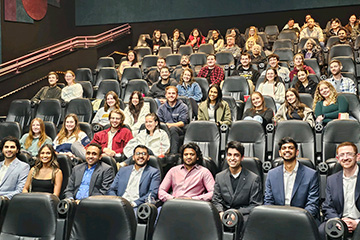 A group medical students sitting in a theater smiling at the camera.