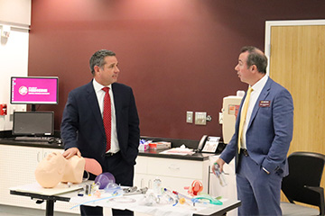 Two men in suits standing at a table of medical equipment having conversation.