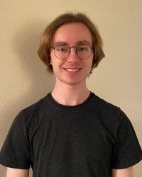 A headshot of Grant Folkert wearing a black t-shirt and glasses.