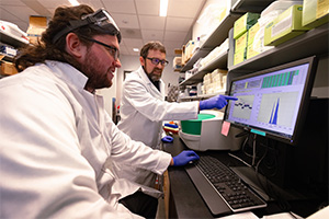 Two male researchers in lab coats analyzing information displayed on a computer monitor.