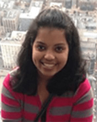 Dr. Bhairavi Srinageshwar with long black hair wearing a red and gray striped sweater smiling at the camera.