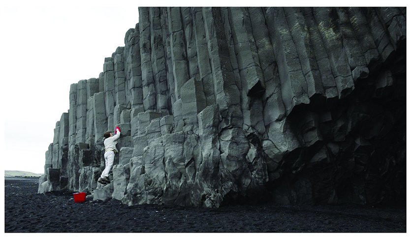 Judy Natal: video still from The Custodian. Person washing the side of a cliff with a bucket and a wash cloth.