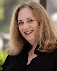 Headshot of Linda Olejniczak wearing black with trees in the background.