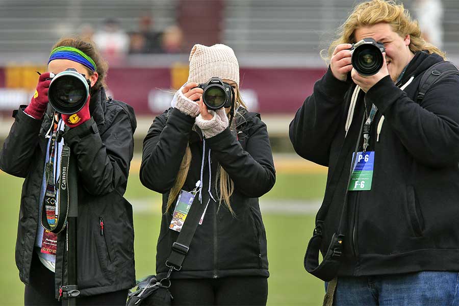 Three Photojournalism students are posing for a photo with their cameras on the field at CMU football stadium Kelly Shorts Stadium on the campus of Central Michigan University.