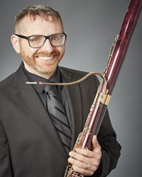 Headshot of Derek Bannasch on a grey backdrop. He's holding his bassoon.