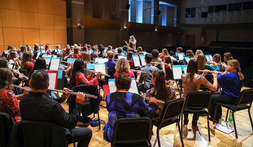 A picture of a flute choir on stage at Staples Family Concert Hall with Dr. Joanna White conducting.