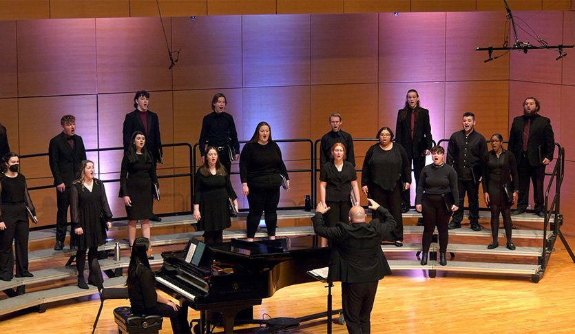 A CMU Choir in black attire performing in Staples Family Concert Hall under the direction of Dr. Amon Eady.