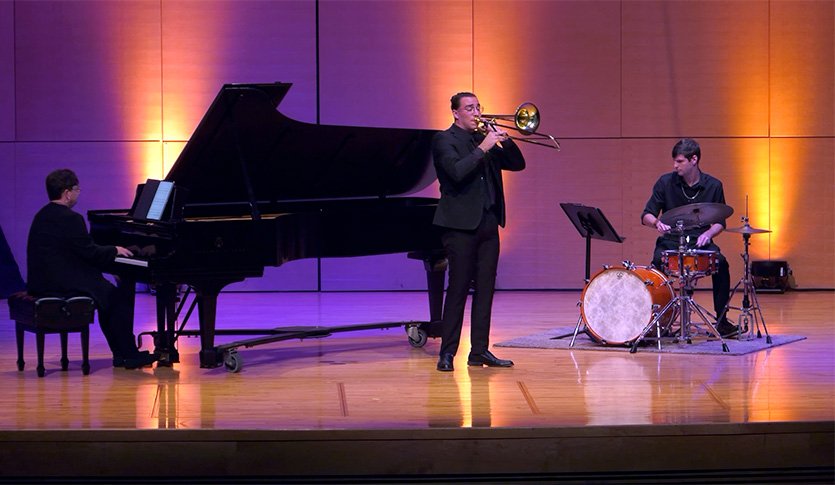 A picture of a pianist, a trombonist, and a drummer in black attire playing at Staples Family Concert Hall.