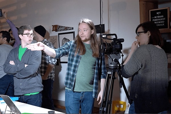 A student directs another student with a camera on how to shoot a scene in the film they are making.