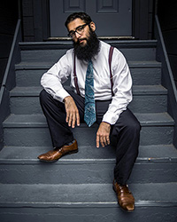 Photo of Jake May dressed in a tie and suspenders, sitting on the stairs.