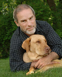 John Grogan and his golden lab Marley posing under a tree on the grass.
