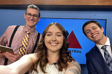 A selfie Kylie Sczepanski has taken with two of her coworkers in front of the CMU News Central logo