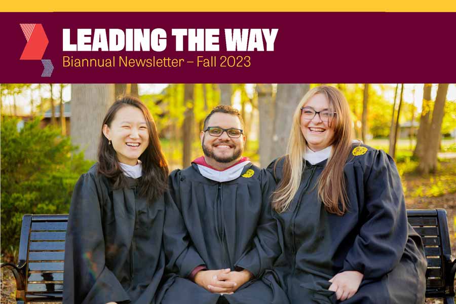 Three graduate students sit on a bench outside in their black commencement robes. There is a headline above the photos that says Leading the Way, Biannual Newsletter - Fall 2023.