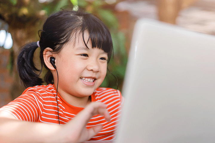 Child in orange striped shirt smiling while looking at a laptop computer