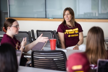 A teacher listening to students having a discussion inside a classroom.