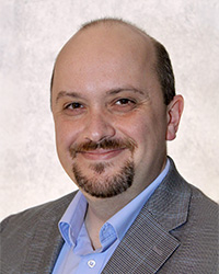 Closeup image of Dennis Hand wearing a blue shirt and grey suit jacket.