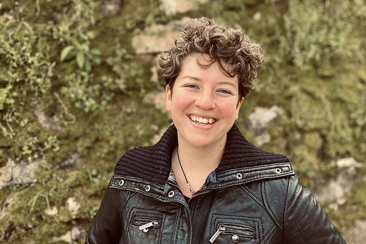 Closeup image of Ashley Schaaf wearing a black jacket and standing in front of green plants.