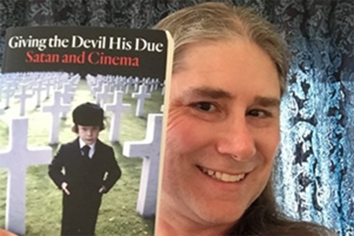 Closeup image of Jeffrey Weinstock holding his book showing a child dressed in black standing between crosses in a cemetery.
