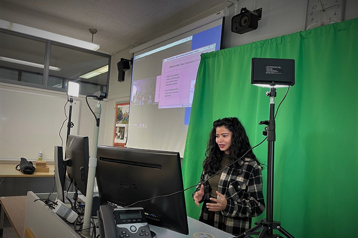 A CMU student standing in front of a green screen presents a live virtual field trip session for the Museum of Cultural and Natural History.