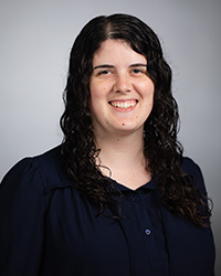 Professional headshot of Allison Peart in a black sweater, smiling against a gray background.