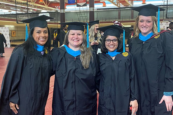 Four Master of Public Administration (MPA) students stand together wearing graduation caps & gowns.