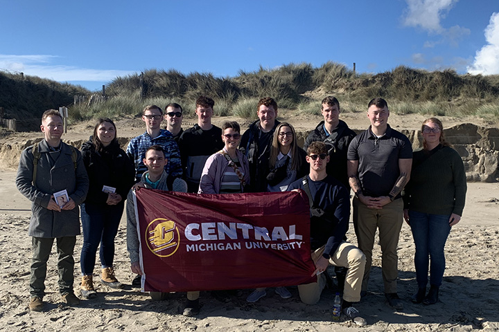 Central Michigan University students hold a CMU flag while posting together at Utah Beach in Normandy, France.