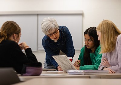 World Languages faculty member Alejandra Rengifo reviews materials with students seated at tables.