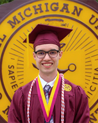 Eric Urbaniak in a maroon cap and gown standing in front of the CMU seal in front of Warriner Hall.